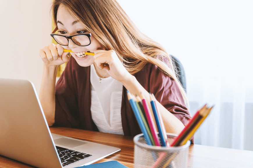 Woman sitting in front of laptop biting yellow pencil.