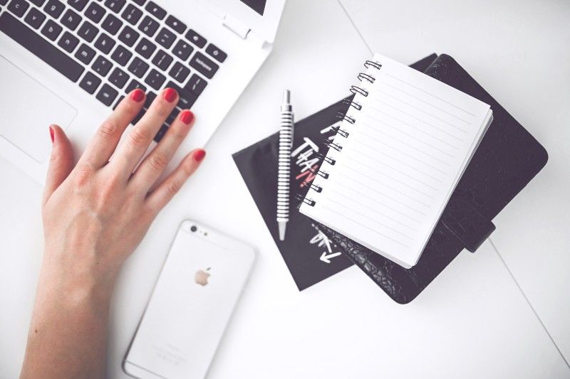 Person sitting at a computer with an Apple iPhone, notebook, and pen.