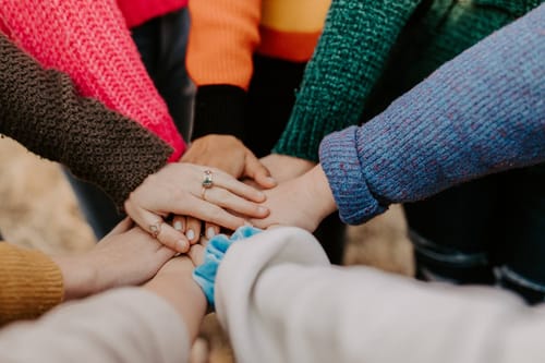 Eight hands laying on top of each other in the middle of a group of people.